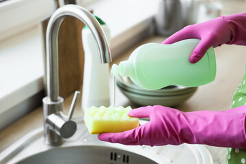 Housewife pouring dish soap onto cleaning sponge in kitchen, closeup