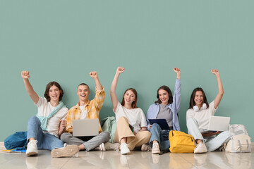 Group of students with laptops and notebooks sitting near green wall