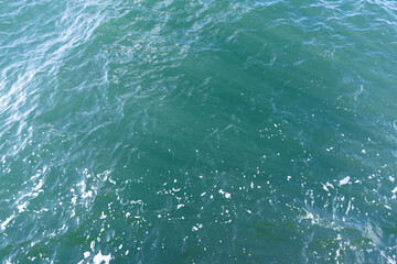 Overhead photo of blue green ocean water with white foam and waves. Background texture