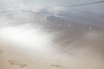 Ocean water on beach sea sand with sun reflection with footprints