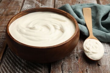 Delicious sour cream in bowl and spoon on wooden table, closeup