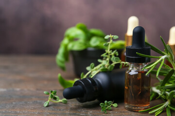 Bottles of aromatic essential oils and herbs on wooden table against brown background, closeup. Space for text