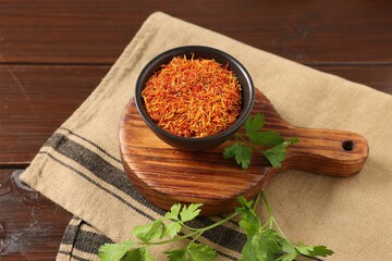 Saffron in bowl and coriander on wooden table, closeup. Aromatic spices