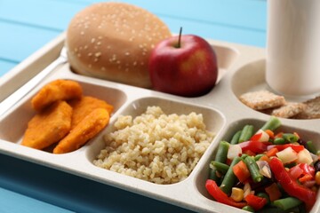 Plastic tray with tasty food and milk on light blue wooden table, closeup. School lunch