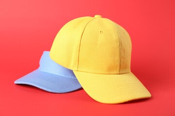Yellow baseball and light blue visor caps on red background, closeup. Mockup for design