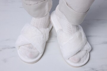 Woman in fluffy slippers on white marble floor, closeup