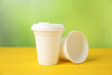 Disposable plastic cups on yellow wooden table against blurred background