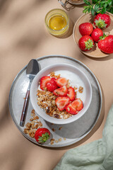 Granola or muesli with natural greek yogurt, strawberry and honey in a bowl on a beige background