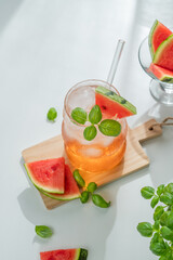 Watermelon mojito cocktail with ice and mint in a glass on a white background with fresh herb and sunlight.