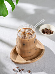 Ice latte coffee in a glass with milk and straw on a wooden plate on light background with coffee beans