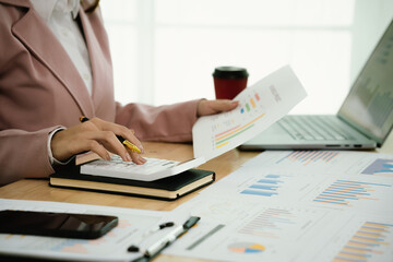 A professional businesswoman reviews financial documents using a calculator, pen, and laptop in the office, analyzing reports, charts, and graphs to manage budget, expenses, investment, and strategic 