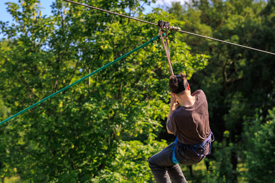 Young caucasian male enjoying zip line adventure in lush green forest - Powered by Adobe
