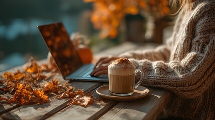 Young woman working on a laptop outside with autumn leaves around. Pumpkin-spice latte on the table, freelance lifestyle