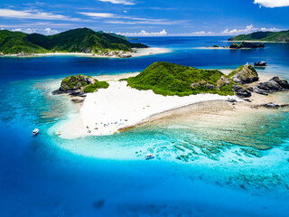 青い海の白砂のビーチが美しい無人島、嘉比島のドローン撮影（沖縄県島尻郡慶良間諸島座間味島嘉比島）
島には白い灯台がある。
座間味島や渡嘉敷島、阿嘉島も見えている。