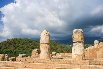 Travel in Turkey. Ancient ruins of Phaselis Ancient City showcase weathered stone columns against a backdrop of lush green hills and dramatic sky, evoking historical significance