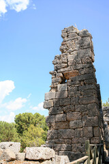 Fototapeta premium Phaselis Ancient City, Turkey. Stone tower ruins showcase ancient architecture in Phaselis Ancient City, surrounded by lush greenery and a clear blue sky