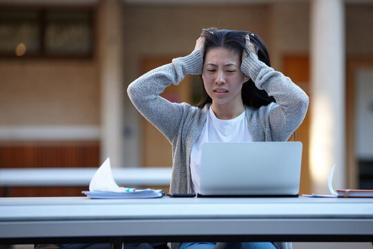 Young Asian university student studying on laptop outdoors stressed