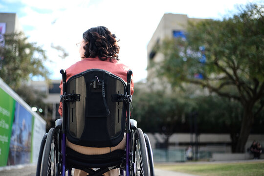 Back shot of a woman with disability sitting in wheelchair outside with trees around her