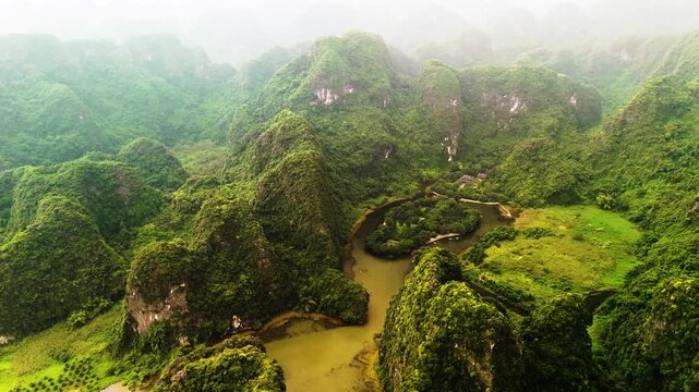 Drone view over the mountains of Ninh Binh, Vietnam. Limestone cliffs are surrounded by rivers and luscious greenery.
