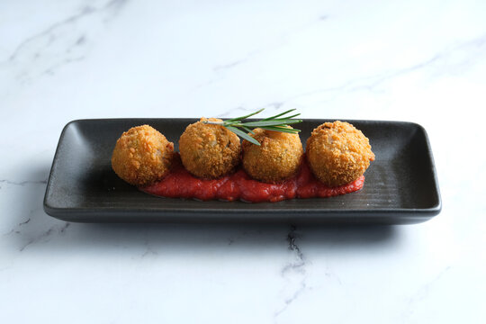 Four golden-brown fried croquettes with red sauce underneath