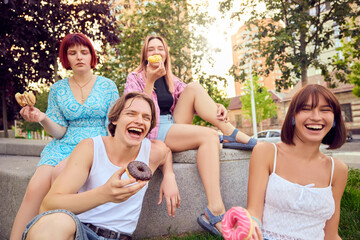 Group of friends laughing and enjoying colorful donuts outdoors on sunny day. Concept of friendship, leisure, street food, summer fun, and joyful social interaction.