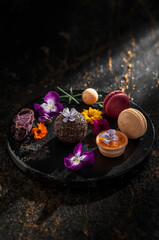 Luxury Gourmet Dessert Assortment with Chocolate Truffles, Macarons, Mini Fruit Tarts, and Edible Flowers on Reflective Black Slate &ndash; Fine Dining, Premium Food Photography
