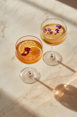 Ultra-Luxury Citrus-Infused Mocktails in Crystal Stemmed Glasses with Floating Edible Flowers and Citrus Slices on Polished White Onyx &ndash; Premium Fine Dining Beverage Photography
