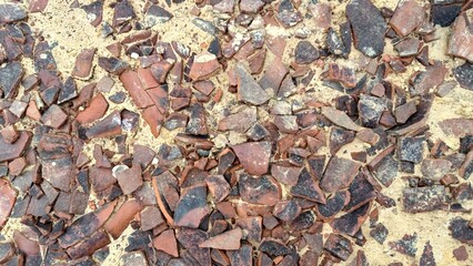 Close-up view of scattered terracotta pottery shards and fragments on sandy ground.