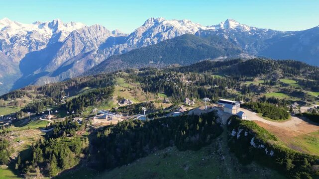 Aerial view of Velika Planina's lush green hills contrasting with snowy mountain peaks under a clear sky, Kamnik, Slovenia.