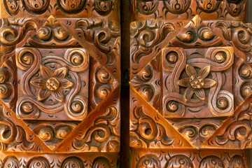 close-up of a wood carving, possibly from an old wooden door or decorative panel, featuring a floral motif in the center surrounded by intricate scrolls and geometric patterns