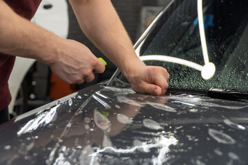 A car wrapping specialist applies a polyurethane film to the car. Detailer smoothes PPF. Car wrapping, detailing, tuning and styling. PPF protective film against chips and scratches. Car protection.