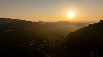 Obraz premium Golden sunrise casting long shadows over the rolling hills, lush orchards, and serene landscapes of Gandia, Spain, creating a picturesque morning scene