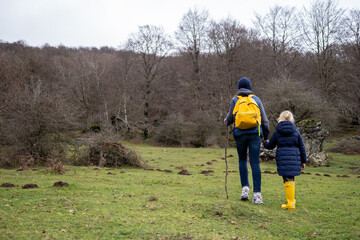 Father, daughter hiking woodland trail, yellow boots matching backpacks, winter landscape surrounding them