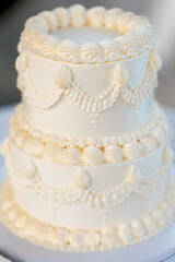 Appetizing small two-tiered wedding cake decorated with cream patterns. Delicate vanilla white cake close-up for wedding or birthday celebration. Concept of elegant festive desserts