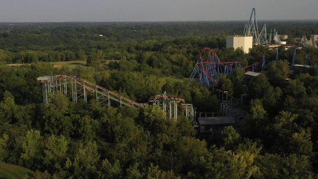 Aerial view of roller coasters weaving through lush green trees, contrasting with the bright colors of the amusement park rides, Mason, Ohio, United States.