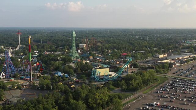 Aerial view of Kings Island amusement park with colorful roller coasters piercing the skyline amidst a sea of lush green trees and expansive parking lots, Mason, Ohio, United States.