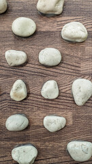 A collection of small white stones arranged on a wood textured surface is suitable for use as a background.