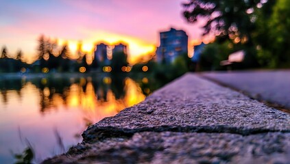 Serene sunset reflected on calm water, city skyline blurred in background, foreground focuses on textured stone