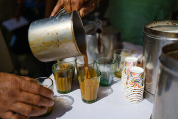Hot Indian chai being poured into glass cups at a roadside tea stall.