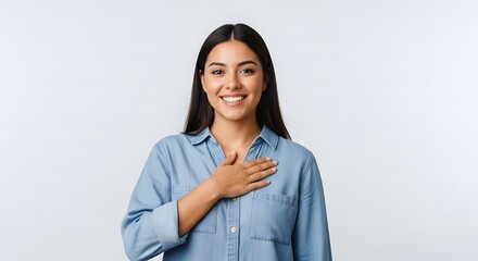 Smiling young woman with a sincere and heartfelt expression placing her hand over her heart, embodying gratitude, honesty, and deep appreciation on a pristine white background.