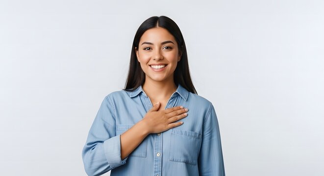 Smiling young woman with a sincere and heartfelt expression placing her hand over her heart, embodying gratitude, honesty, and deep appreciation on a pristine white background.