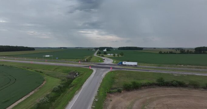 Aerial view of a stark intersection with a truck passing by, surrounded by vibrant green fields under a cloudy sky, Monroeville, Indiana, United States.