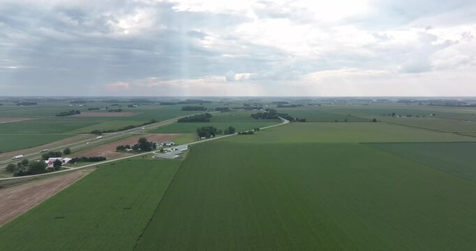 Aerial view of patchwork farmland, bisected by roads, contrasting shades of green, under a cloudy sky, Monroeville, Indiana, United States.