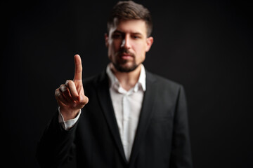 Business professional in formal attire signaling a message with a raised finger in a dark setting