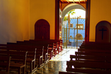 Sunlight streams through a wrought iron gate into a quiet church interior, casting warm patterns on...
