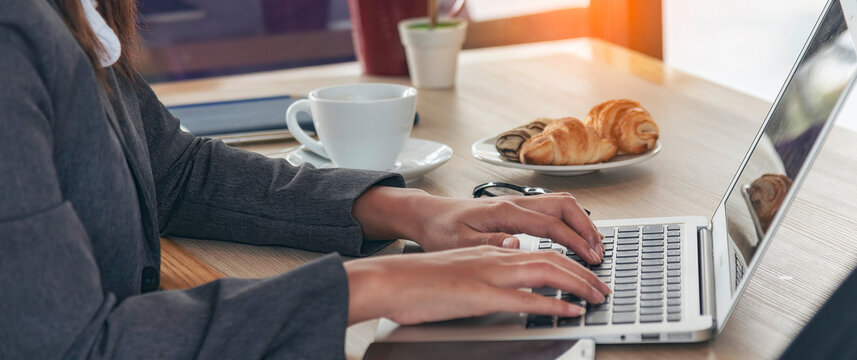 Close up businesswoman hand typing laptop drink black coffee cup in green garden cafe. Woman Hands love drinking hot coffee working from home. Business women with black coffee or hot chocolate cafe