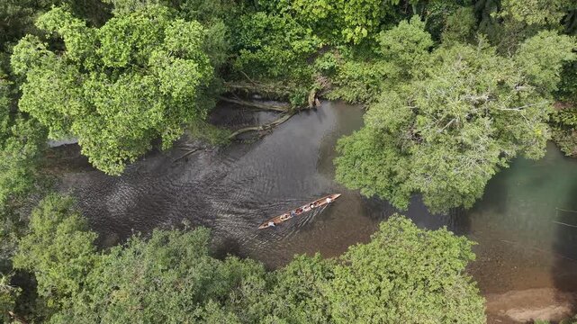 Aerial view of a boat gliding through the river, surrounded by vibrant green trees, creating a serene contrast of light and shadow, Nuqu&iacute;, Choco, Colombia.