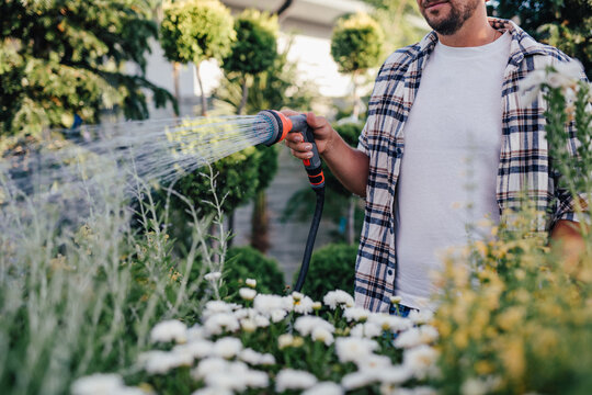 Close up of garden center worker watering plants with hose in greenhouse.