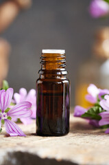 A brown bottle of common mallow essential oil with blooming malva sylvestris plant