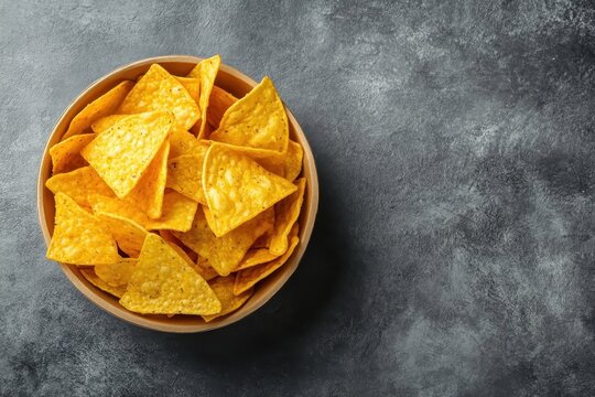 top view of yellow corn chips in kraft paper bowl on grey background.